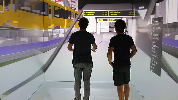 Two persons watch a train arrive in virtual reality.