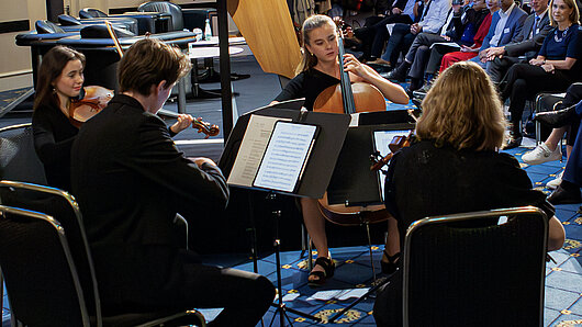A string quartet plays in the foreground, with event attendees in the background.