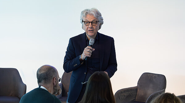 A man stands in front of a room and speaks into a microphone.