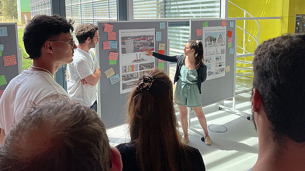 A woman standing in front of a poster explains her plans to a group of colleagues.