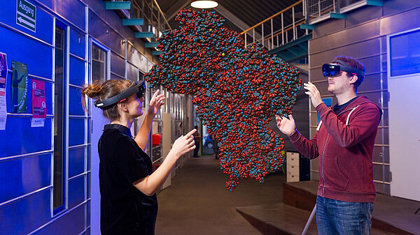 Photo of a man and a woman wearing 3D glasses, which visualize an object in the air between them.