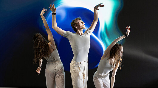 Three dancers in front of a large, colorful LED screen.