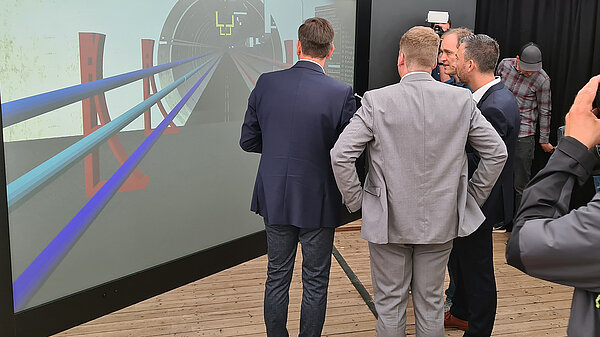Foto von Menschen, die bei der Feier in Glückstadt die Visualisierung des ElbX-Tunnels betrachten.