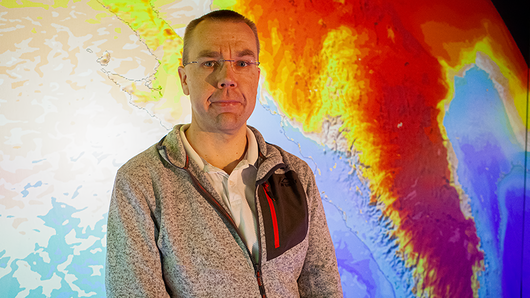 Portrait of Thomas Schwitalla in front of a visualization of his weather model.