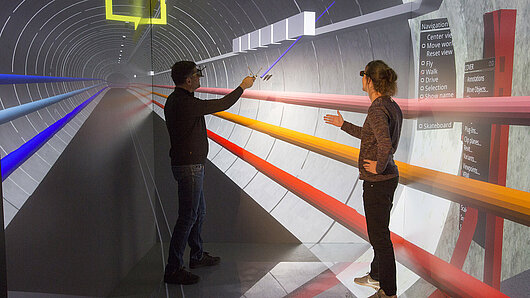 Photo of two people in the CAVE virtual reality facility observing the layout of electrical cables passing through the ElbX tunnel.