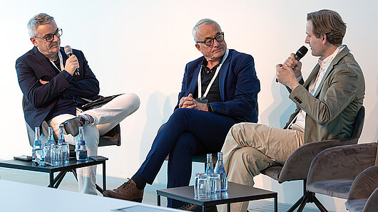 Three men converse in a podium discussion.