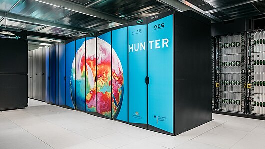 Photo of HLRS's Hunter supercomputer, with image of Earth weather simulation on the side of the machine.. Copyright: Julian Holzwarth/HLRS