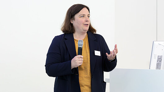 A woman holds a microphone while giving a lecture.