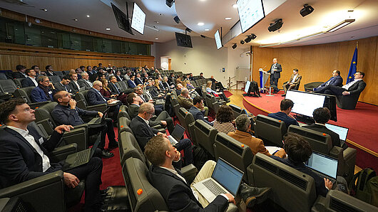 Full auditorium with speakers on stage, photographed from the side of the auditorium.