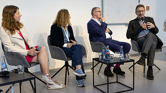 Four individuals sit in chairs for a panel discussion.
