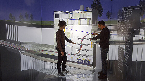 Foto von zwei Personen in der CAVE Virtual-Reality-Anlage, die eine Visualisierung eines ElbX-Kontrollgebäudes untersuchen.