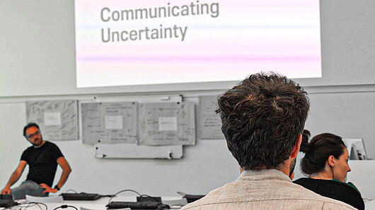 Photo of auditorium during the conference, with the phrase "Communicating Uncertainty" on the screen.